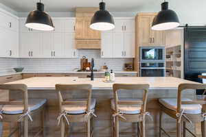 Kitchen with stainless steel appliances, decorative backsplash, light countertops, a kitchen island with sink, and a breakfast bar