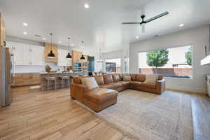 Living room featuring recessed lighting, light wood-style flooring, a ceiling fan, baseboards, and a textured ceiling