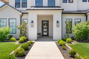 View of exterior entry with a standing seam roof, stucco siding, a yard, and metal roof