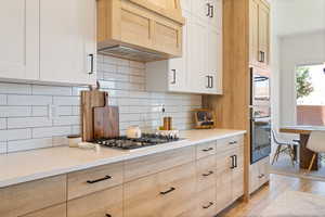 Kitchen featuring custom range hood, light wood-style floors, backsplash, light countertops, and stainless steel gas cooktop