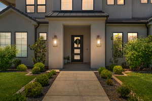 Doorway to property featuring a standing seam roof, stucco siding, a lawn, and metal roof