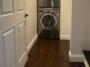 Laundry area with stacked washer / dryer, dark wood-type flooring, and baseboards