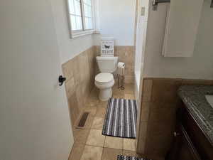 Bathroom with tile walls, tile patterned flooring, vanity, toilet, and a wainscoted wall