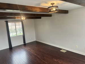Unfurnished room featuring beam ceiling, dark wood finished floors, and baseboards