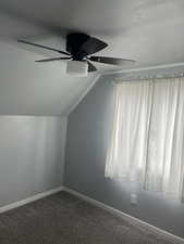 Additional living space featuring ceiling fan, vaulted ceiling, baseboards, and dark colored carpet