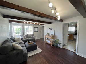 Living area with wood finished floors, beamed ceiling, baseboards, and rail lighting