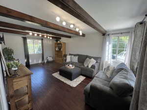 Living area with plenty of natural light, beamed ceiling, dark wood-type flooring, and baseboards
