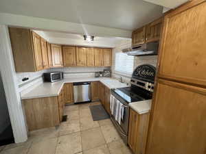 Kitchen with appliances with stainless steel finishes, under cabinet range hood, tasteful backsplash, and light countertops