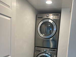 Washroom with stacked washer and clothes dryer, dark wood-type flooring, and baseboards