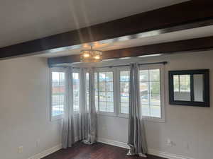 Unfurnished room featuring beamed ceiling, dark wood-style flooring, and baseboards