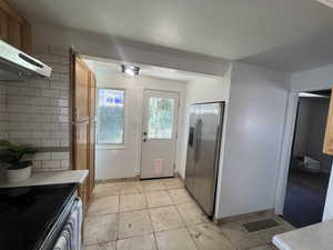 Kitchen featuring stainless steel appliances, range hood, light countertops, decorative backsplash, and brown cabinets