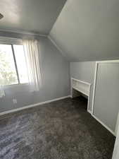 Bonus room featuring vaulted ceiling, dark carpet, and baseboards