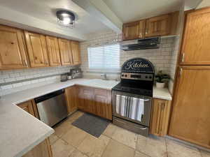 Kitchen with extractor fan, stainless steel appliances, a sink, decorative backsplash, and light countertops