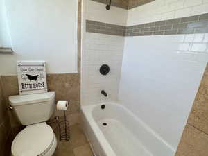 Full bath with toilet, tile walls, bathing tub / shower combination, tile patterned floors, and wainscoting