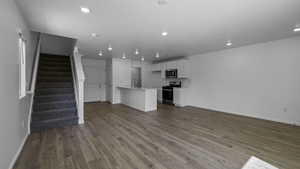 Unfurnished living room featuring baseboards, dark wood-type flooring, stairway, a sink, and recessed lighting