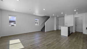 Unfurnished living room featuring recessed lighting, healthy amount of natural light, dark wood-style flooring, stairway, and baseboards