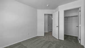 Unfurnished bedroom featuring dark colored carpet, baseboards, a closet, and a spacious closet