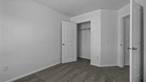 Unfurnished bedroom featuring dark colored carpet, baseboards, and a closet