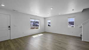 Unfurnished living room featuring plenty of natural light, stairs, wood finished floors, a textured ceiling, and recessed lighting