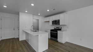 Kitchen with appliances with stainless steel finishes, a sink, a peninsula, dark wood finished floors, and baseboards