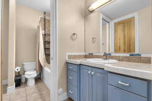Bathroom featuring vanity, tile patterned flooring, shower / bath combination with curtain, and toilet