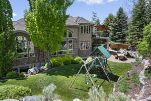 Back of property featuring stone siding, a patio, a playground, a lawn, and a balcony