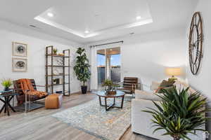Living area with wood finished floors, recessed lighting, a tray ceiling, and baseboards