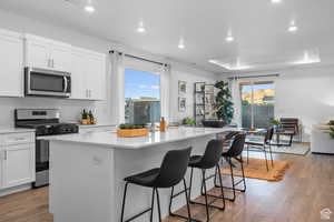 Kitchen featuring stainless steel appliances, an island with sink, a breakfast bar, wood finished floors, and recessed lighting