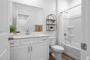 Bathroom with toilet, wood finished floors, vanity, and shower / bathtub combination with curtain