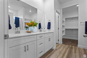 Full bath with double vanity, wood finished floors, a walk in closet, and recessed lighting