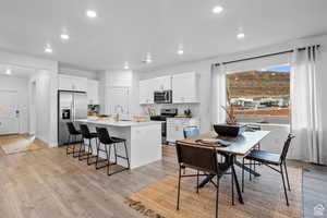 Kitchen featuring appliances with stainless steel finishes, a sink, a center island with sink, recessed lighting, and a breakfast bar