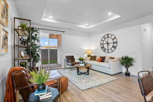 Living room with wood finished floors, a raised ceiling, recessed lighting, and baseboards