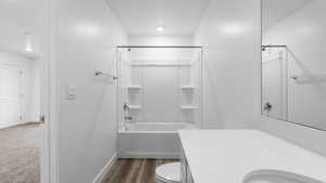 Bathroom featuring bathing tub / shower combination, toilet, vanity, baseboards, and wood finished floors