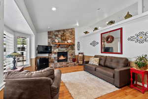 Living room featuring vaulted ceiling, a stone fireplace, and light wood finished floors