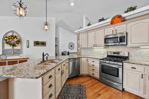 Kitchen featuring stainless steel appliances, a sink, a peninsula, backsplash, and vaulted ceiling