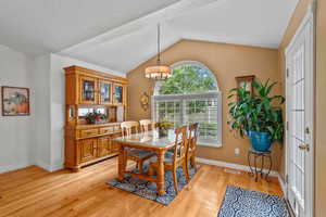 Dining space with vaulted ceiling, light wood-style flooring, baseboards, and a chandelier
