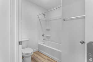 Full bath featuring wood finished floors, toilet, shower / washtub combination, and baseboards