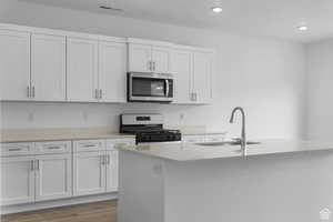 Kitchen with stainless steel microwave, gas stove, a sink, light countertops, and a kitchen island with sink