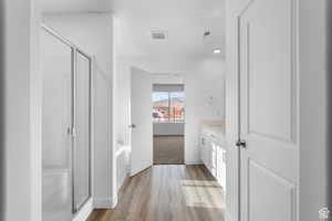 Bathroom featuring a stall shower, a bath, baseboards, wood finished floors, and vanity