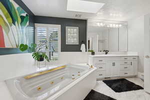 Bathroom with a skylight, a whirlpool tub, vanity, marble finish floors, and toilet