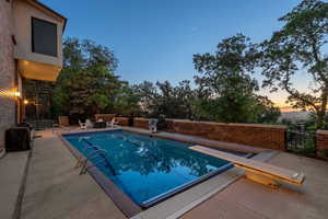Pool at dusk featuring a patio area and a diving board