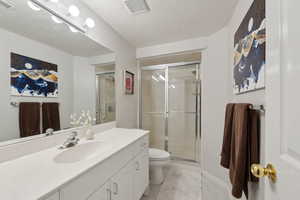 Bathroom with vanity, tile patterned flooring, toilet, a shower stall, and a textured ceiling