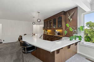 Kitchen featuring dark carpet, glass insert cabinets, a kitchen breakfast bar, baseboards, and light countertops