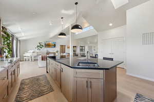 Kitchen with a sink, light wood finished floors, vaulted ceiling, baseboards, and a kitchen island with sink