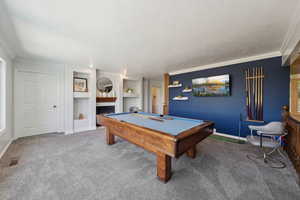 Playroom with carpet floors, a warm lit fireplace, built in features, billiards, and ornamental molding