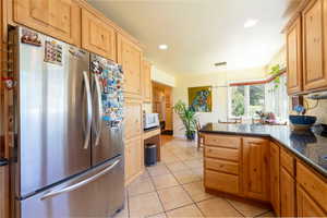 Kitchen featuring freestanding refrigerator, white microwave, light tile patterned floors, a peninsula, and dark stone countertops
