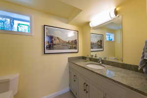 Half bathroom with toilet, plenty of natural light, vanity, and baseboards