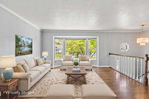 virtually staged Living area featuring wood finished floors, a chandelier, crown molding, baseboards, and a textured ceiling