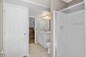 Full bathroom with a stall shower, vanity, ornamental molding, tile patterned flooring, and toilet