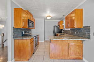 Kitchen with black appliances, a sink, a textured ceiling, light stone countertops, and a peninsula